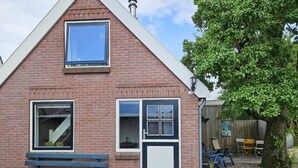 Une maison en briques avec un toit à pignon, une fenêtre, une porte et un banc à l’extérieur.