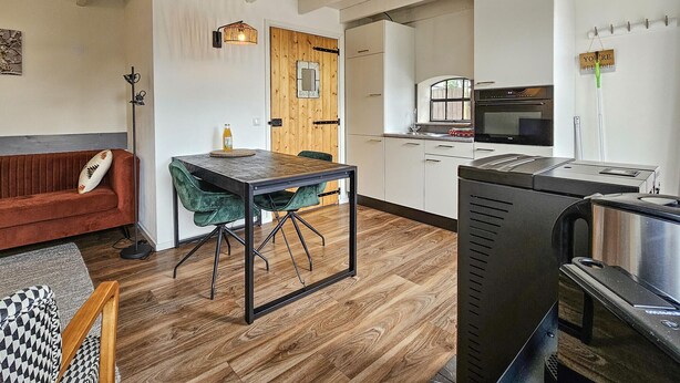 Une cuisine compacte dotée d’appareils électroménagers modernes, un coin repas avec une table et des chaises en bois, et un coin salon confortable avec un canapé rouge.