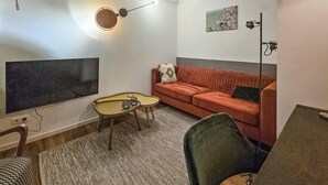 Un salon moderne avec un canapé, une petite table ronde, un téléviseur et une lampe fixée au mur.