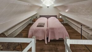 Une chambre avec deux lits, un plancher en bois, des murs blancs et un plafond en pente.