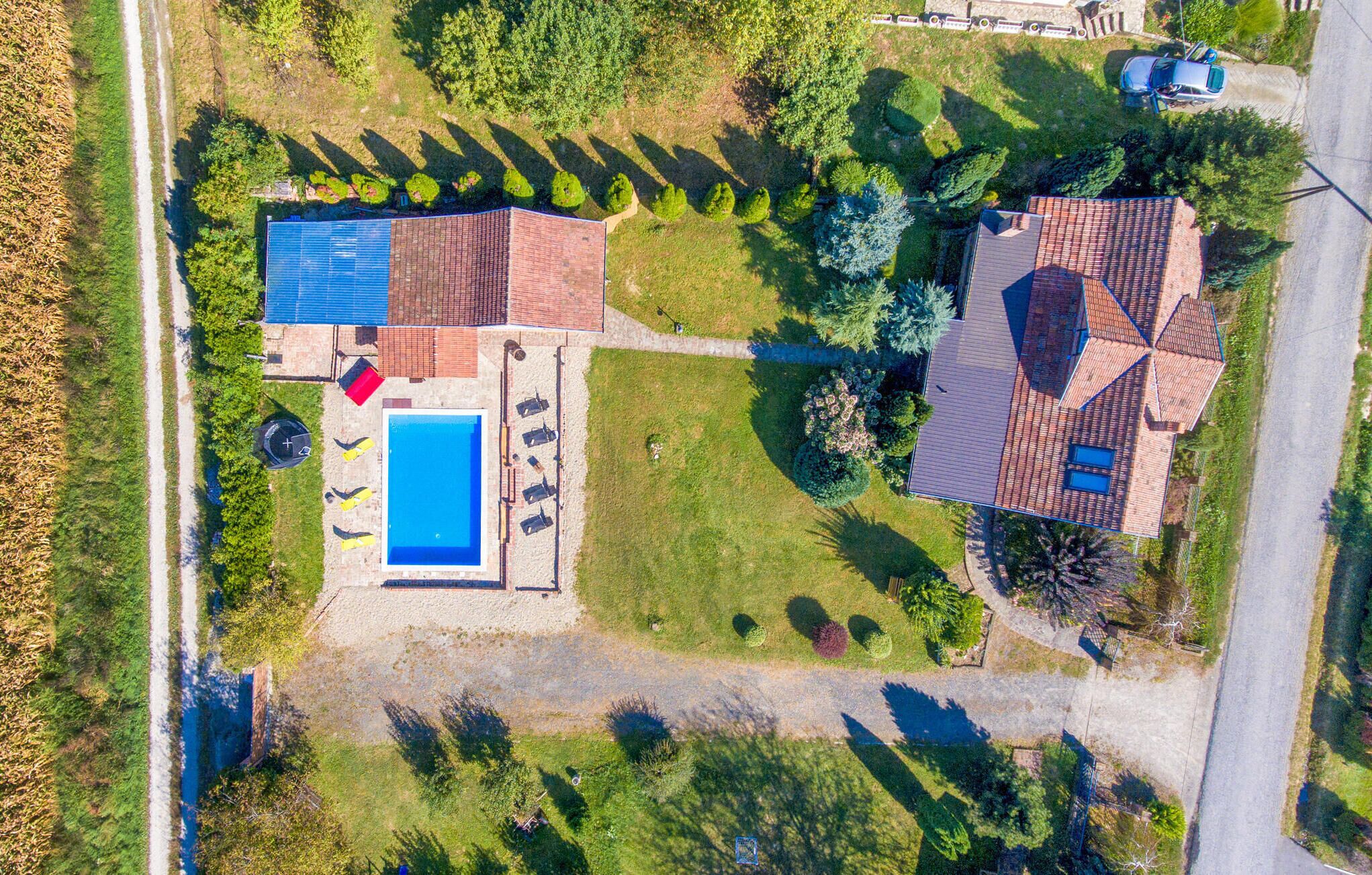 Luchtbeeld van een woonhuis met zwembad, tennisbaan en een verzorgde tuin.