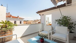 Ein Balkon mit Glastisch, weißen Stühlen und Topfpflanzen.