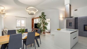 Eine moderne Küche mit einer zentralen Kochinsel, einem Essbereich mit Holztisch und Stühlen sowie einer großen Kübelpflanze.