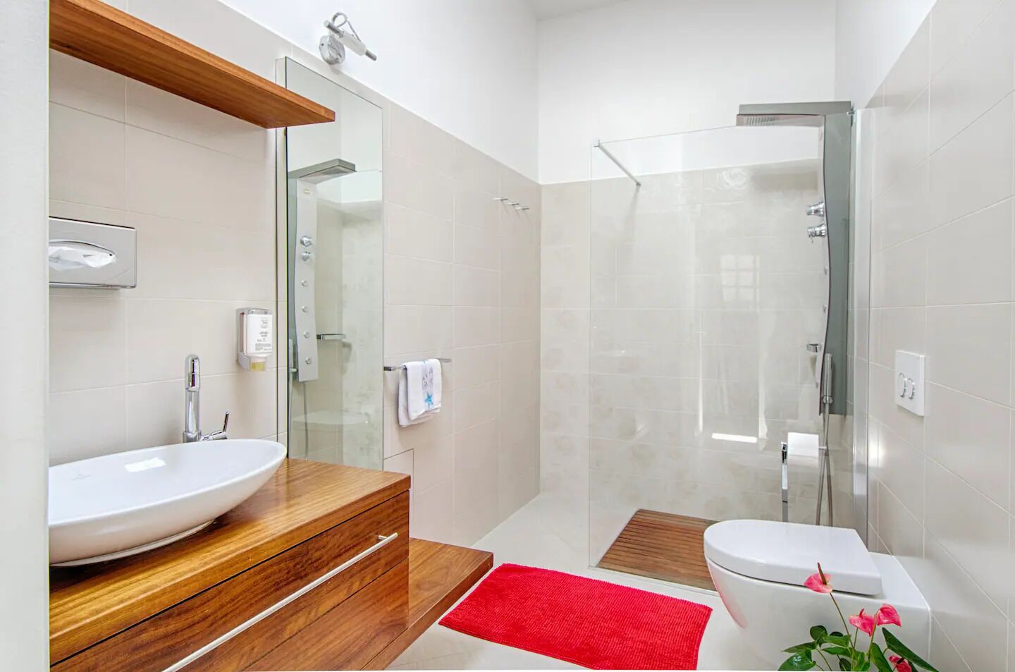 Une salle de bain moderne avec un grand lavabo blanc, un meuble-lavabo en bois, une cabine de douche en verre et un tapis de bain rouge.