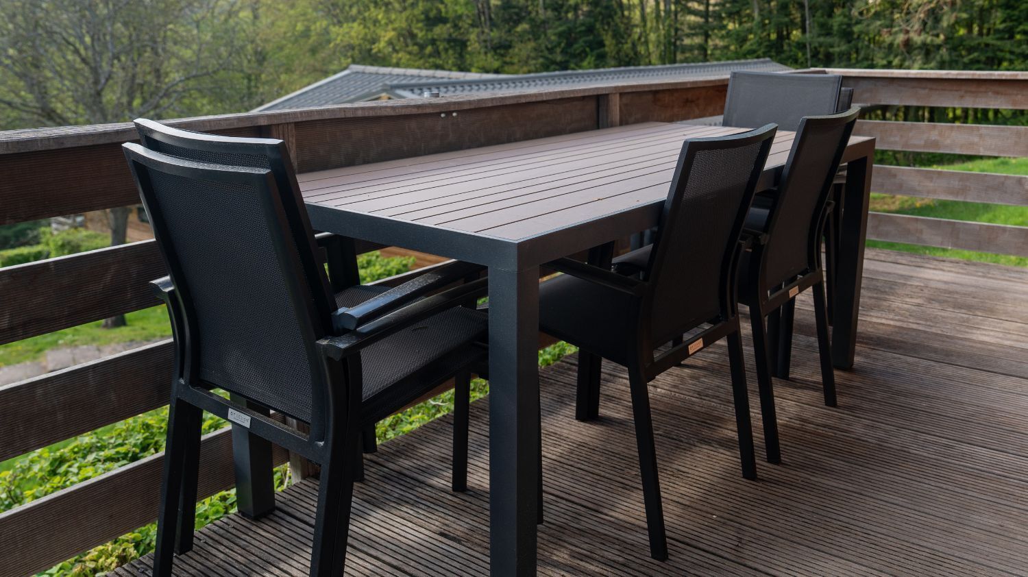 Une terrasse en bois avec une table et des chaises, entourée d’une balustrade en bois.