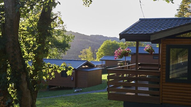 Une rangée de chalets en bois dotés d’un balcon, entourés d’arbres et avec une chaîne de montagnes en arrière-plan.