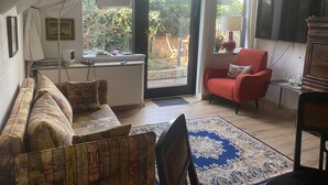 A living room with a sofa, a red armchair, a television, and a large window with curtains. - Stylishly furnished apartment in a modern half-timbered house-children welcome! (Bremen)