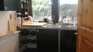 A compact kitchen with a sink, a countertop, and a built-in oven. There are hanging lights above the sink and a window providing natural light. - Stylishly furnished apartment in a modern half-timbered house-children welcome! (Bremen)