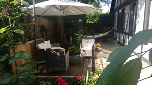 A garden patio with a wooden deck, a white umbrella, wicker furniture, and various plants and flowers. - Stylishly furnished apartment in a modern half-timbered house-children welcome! (Bremen)