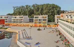 A modern building with multiple floors, outdoor seating areas, and a central open space. - Dünenvilla 14, Whg 4 (Travemünde Waterfront)