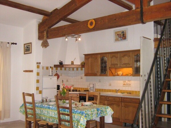 Un coin repas avec une table dressée pour quatre personnes, des chaises en bois et, au fond, une cuisine dotée de meubles en bois et d’un dosseret carrelé.