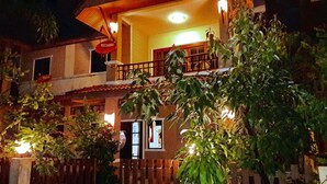 Un edificio de dos plantas con un balcón, una valla de madera y un letrero rojo.