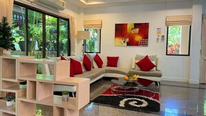Un salón moderno con un sofá, cojines rojos, una mesa de centro con fruta y un amplio ventanal con vistas a zonas verdes.