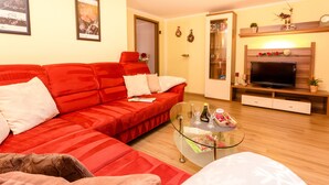 Una sala de estar con un sofá rojo, una mesa de centro de vidrio y un televisor de pantalla plana sobre un soporte de madera.