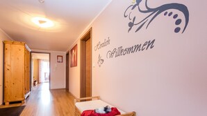 Un pasillo con un banco de madera, una cama con una manta roja y una pared con un cartel de bienvenida.