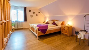Un dormitorio con una cama de madera, una mesita de noche, un radiador, una ventana con cortinas y una pared decorada con adornos de corazón.