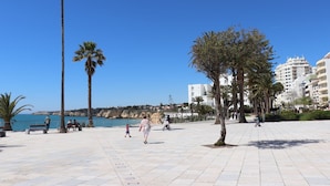 A paved promenade with palm trees, benches, and a clear view of the sea and buildings in the background. - Exceptional apartment seafront (Armação de Pera)