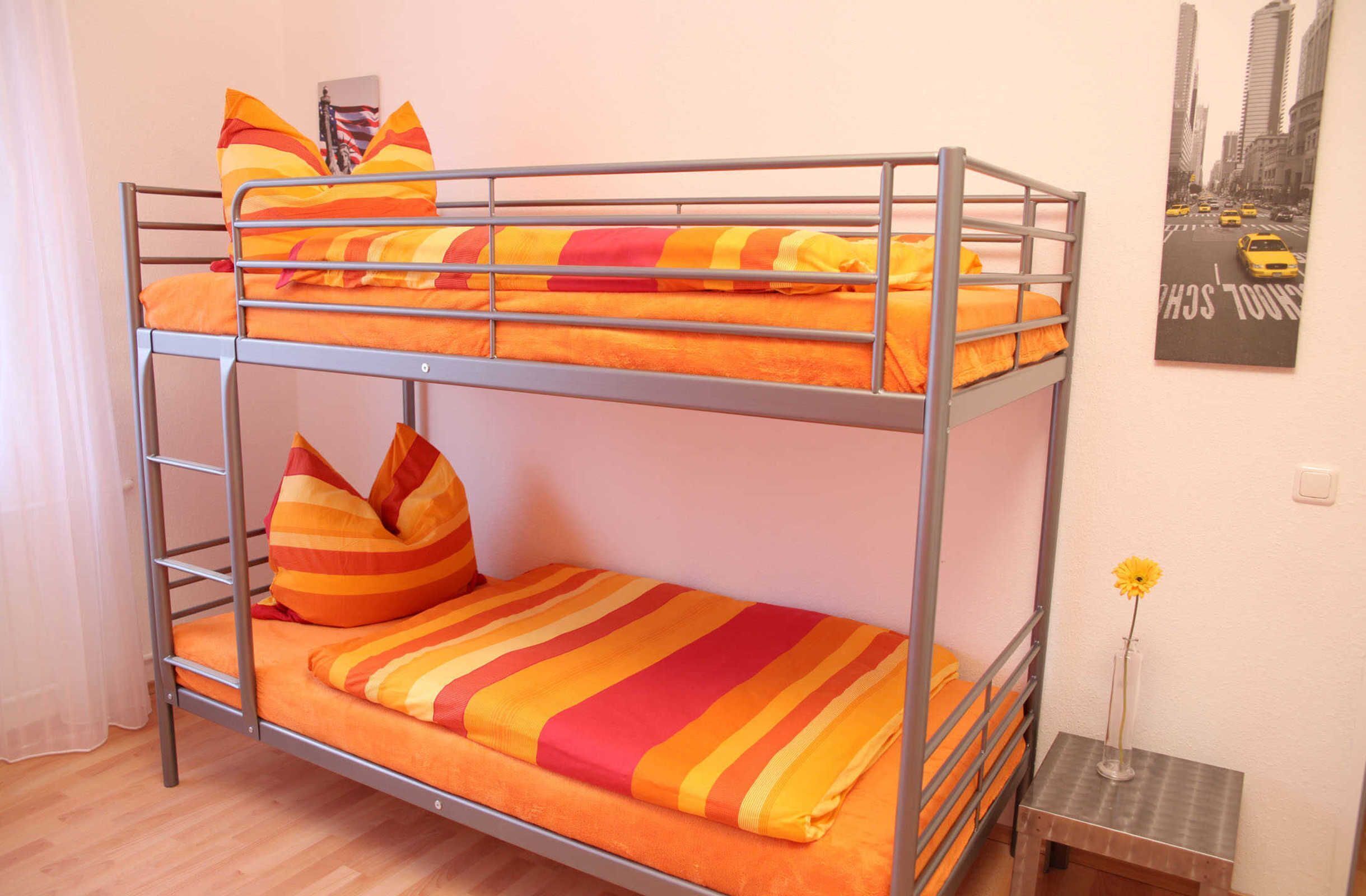 Ein Stockbett mit orangefarbener Bettwäsche und gestreiften Kissen.