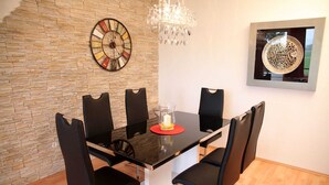 A dining area with a stone wall, a round wall clock, a chandelier, and a framed artwork.