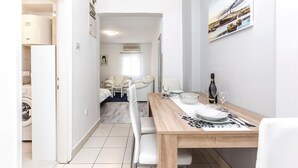 Ett modernt matområde med ett träbord dukat för två personer, en soffa och utsikt över en hamn med båtar.