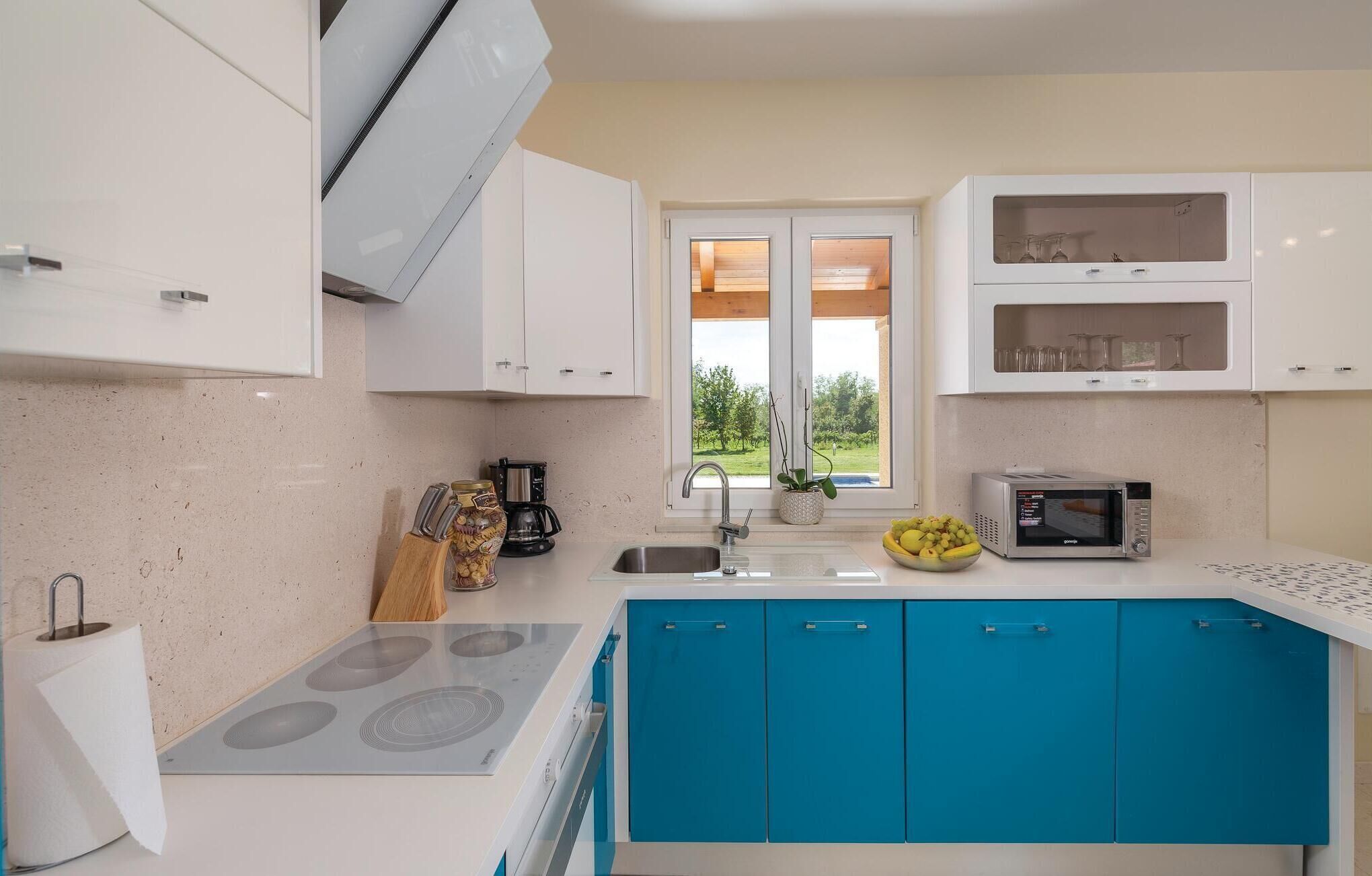 Une cuisine moderne avec des meubles blancs et bleus, une cuisinière encastrée, un four à micro-ondes et une machine à café.