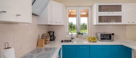 Une cuisine moderne avec des meubles blancs et bleus, une cuisinière encastrée, un four à micro-ondes et une machine à café.