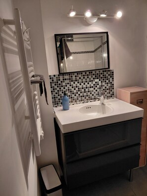 A bathroom with a white sink, a mirror, a black tiled backsplash, and a black cabinet. - L'Appart, charm and confort  (Cotignac)