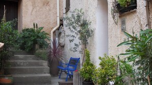 A narrow courtyard with steps leading to a door, surrounded by potted plants and a blue chair. - L'Appart, charm and confort  (Cotignac)