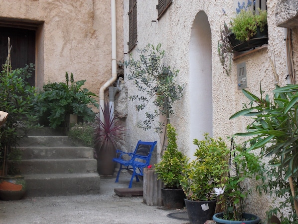 A narrow courtyard with steps leading to a door, surrounded by potted plants and a blue chair. - L'Appart, charm and confort (Cotignac)