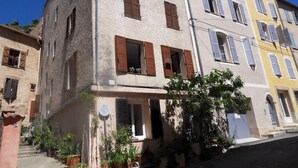 A multi-story building with a mix of window styles and shutters, a visible entrance, and potted plants in the foreground. - L'Appart, charm and confort  (Cotignac)