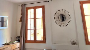 A room with a ceiling fan, a window with curtains, a wall-mounted mirror, and a radiator. - L'Appart, charm and confort  (Cotignac)