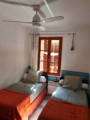 A room with two beds, a ceiling fan, a window with wooden shutters, and a radiator. - L'Appart, charm and confort  (Cotignac)
