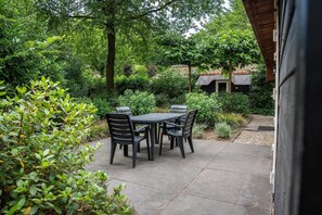 Eine Außenpatio mit Tisch und Stühlen, umgeben von üppiger Vegetation und einem Haus im Hintergrund.