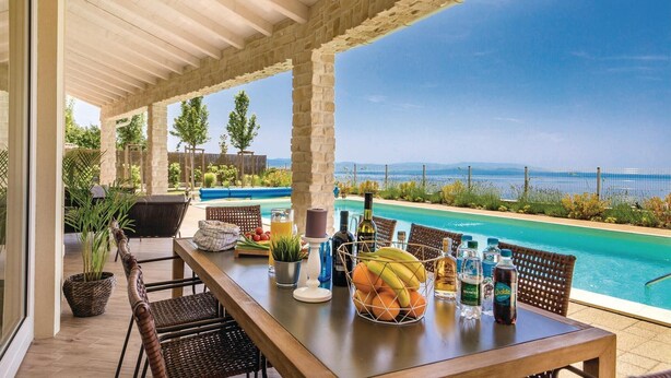 A covered outdoor dining area with a pool view, featuring a wooden table, wicker chairs, and a variety of beverages and fruits. - Amazing home in Veprinac with sauna (Veprinac)