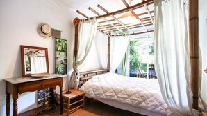 Een kamer met een bed, een houten nachtkastje, een spiegel en een raam met gordijnen.