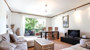 Een woonkamer met een bank, een salontafel, een televisie en een eethoek met stoelen.