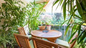 Een ronde houten tafel met stoelen, omringd door potplanten, op een balkon met uitzicht op groen.