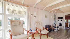 A spacious living area with a large window, a wooden ceiling, and a cozy seating arrangement including a sofa and two armchairs.