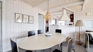 A dining area with a round table, black chairs, a hanging pendant light, and framed artwork on the wall.