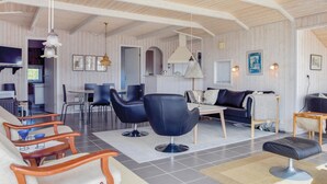A spacious living area with a high ceiling, wooden panel walls, a dining table with chairs, a sofa, and a coffee table.