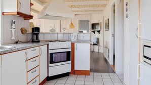 A kitchen with white cabinets, a stove, and a microwave. There is a wooden ceiling and a tiled floor.