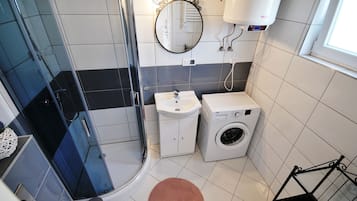 A modern bathroom with a glass shower enclosure, a sink, a washing machine, and a mirror.