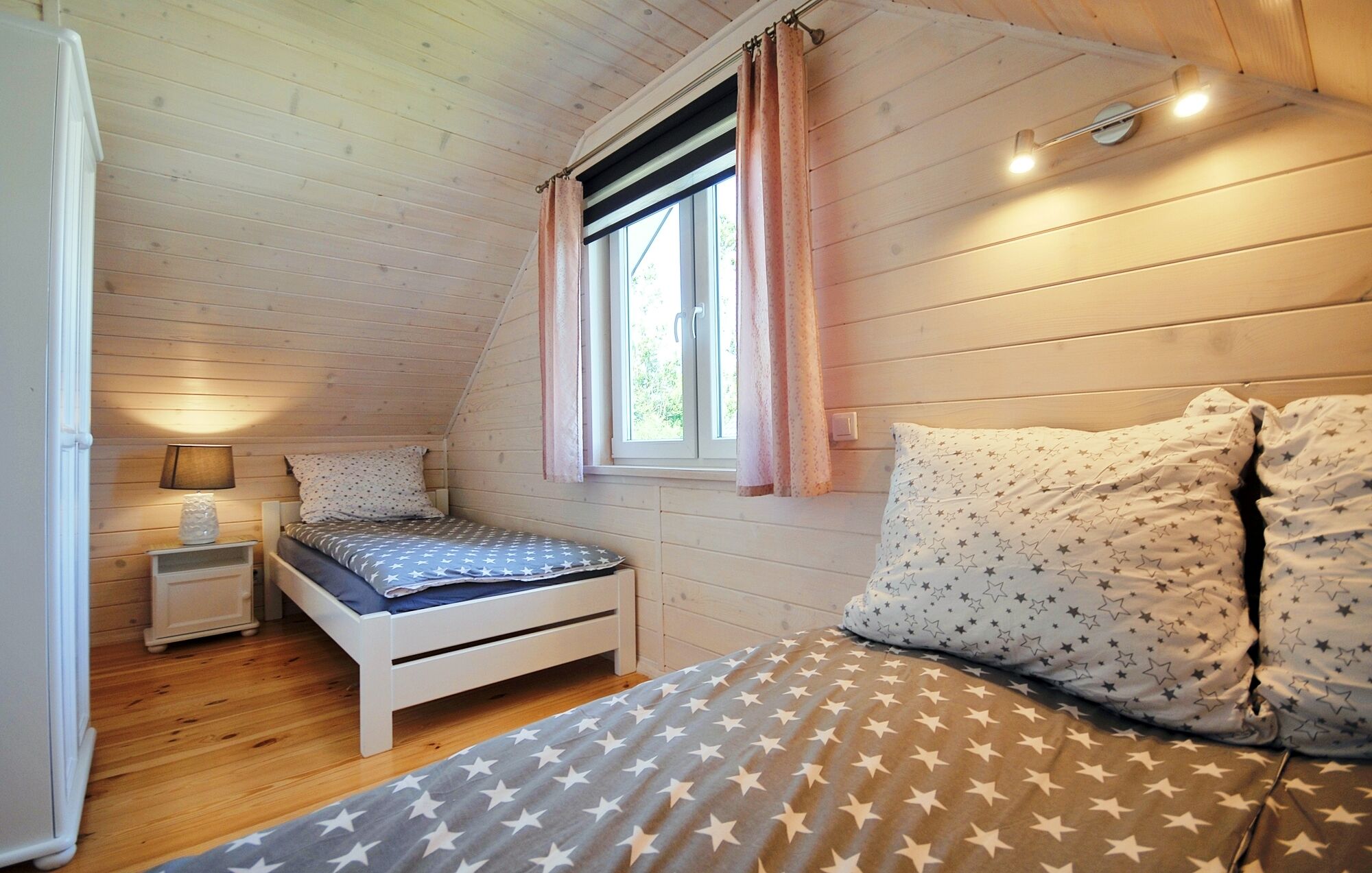 A cozy bedroom with a single bed, a nightstand, a lamp, and a window with curtains.
