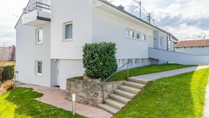 Uma casa moderna de dois andares com uma escadaria de pedra que leva à entrada, um gramado bem cuidado e um céu limpo.