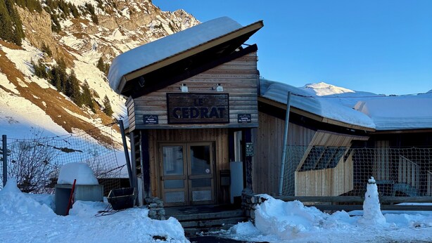 Una cabaña de madera en la montaña llamada "Le Cedrat" con techo cubierto de nieve, fachada de madera y un cartel que indica que es un refugio de montaña.