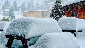 Un espacio exterior cubierto de nieve con un banco de madera y un edificio al fondo.