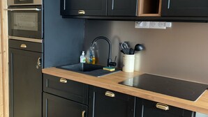 Una cocina moderna con armarios oscuros, encimera de madera y electrodomésticos integrados, incluyendo un horno y un fregadero.