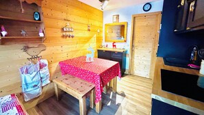 Una habitación pequeña y acogedora con detalles de madera, una mesa de madera con mantel rojo, un banco, un espejo sobre un lavamanos y un reloj en la pared.