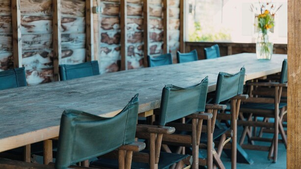 A rustic wooden table with matching chairs, set against a stone wall. - Group farm for 20 people (Voorthuizen)