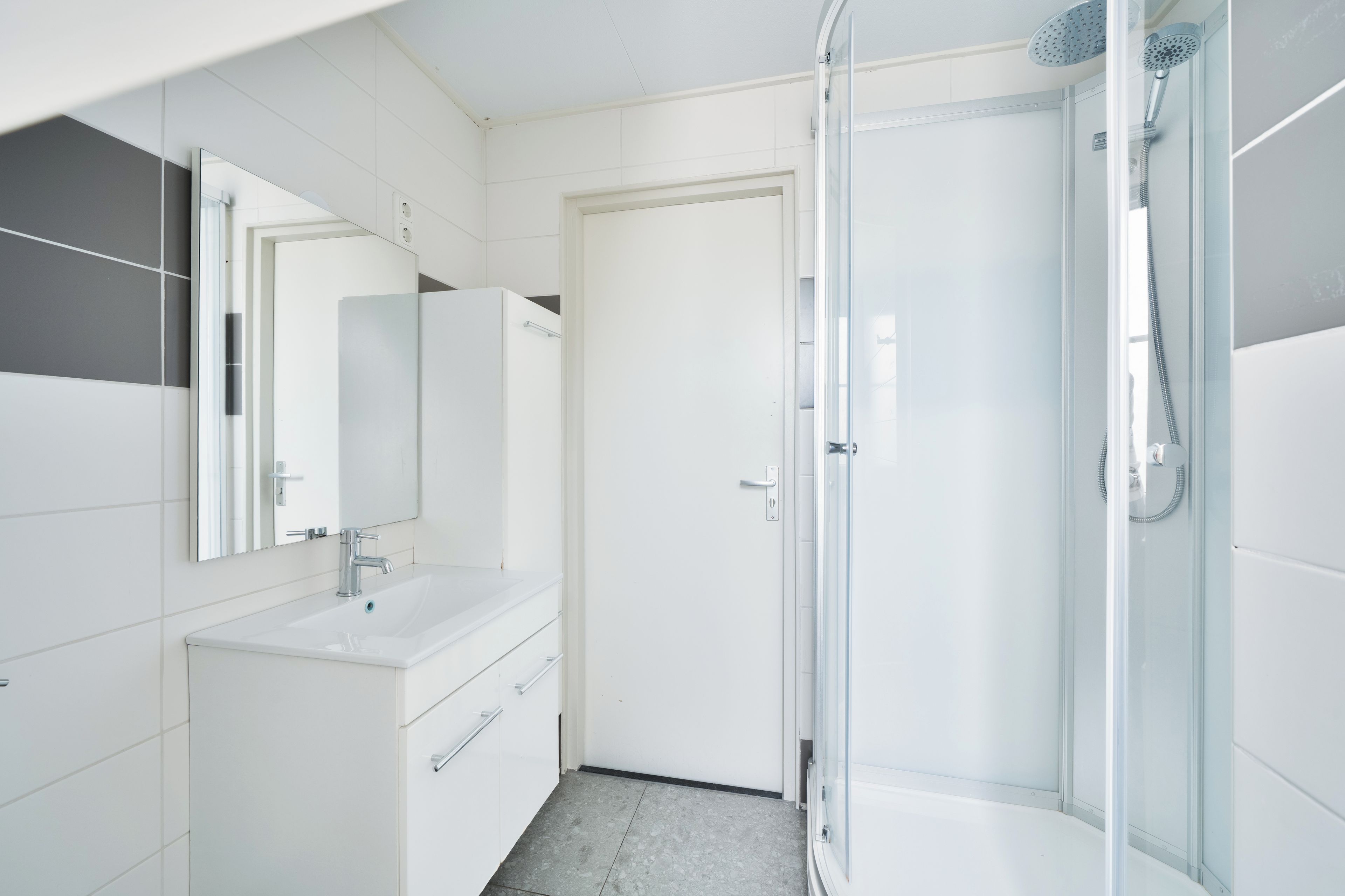 A modern bathroom with a glass-enclosed shower, a white sink, and a mirror above it.